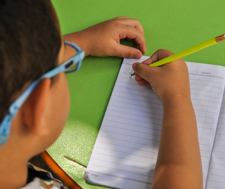 Young boy writing in a composition notebook on a green table